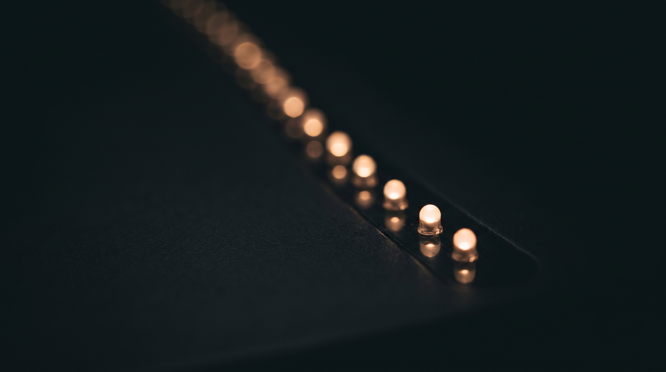 Extreme close-up of a row of small amber-white charging indicator lights receding diagonally into soft darkness, sharp in the foreground and blurring into black toward the back, no people, casing or room visible.